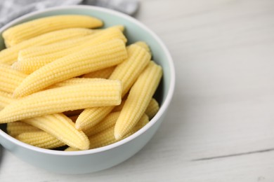 Photo of Tasty fresh yellow baby corns in bowl on white wooden table, closeup. Space for text