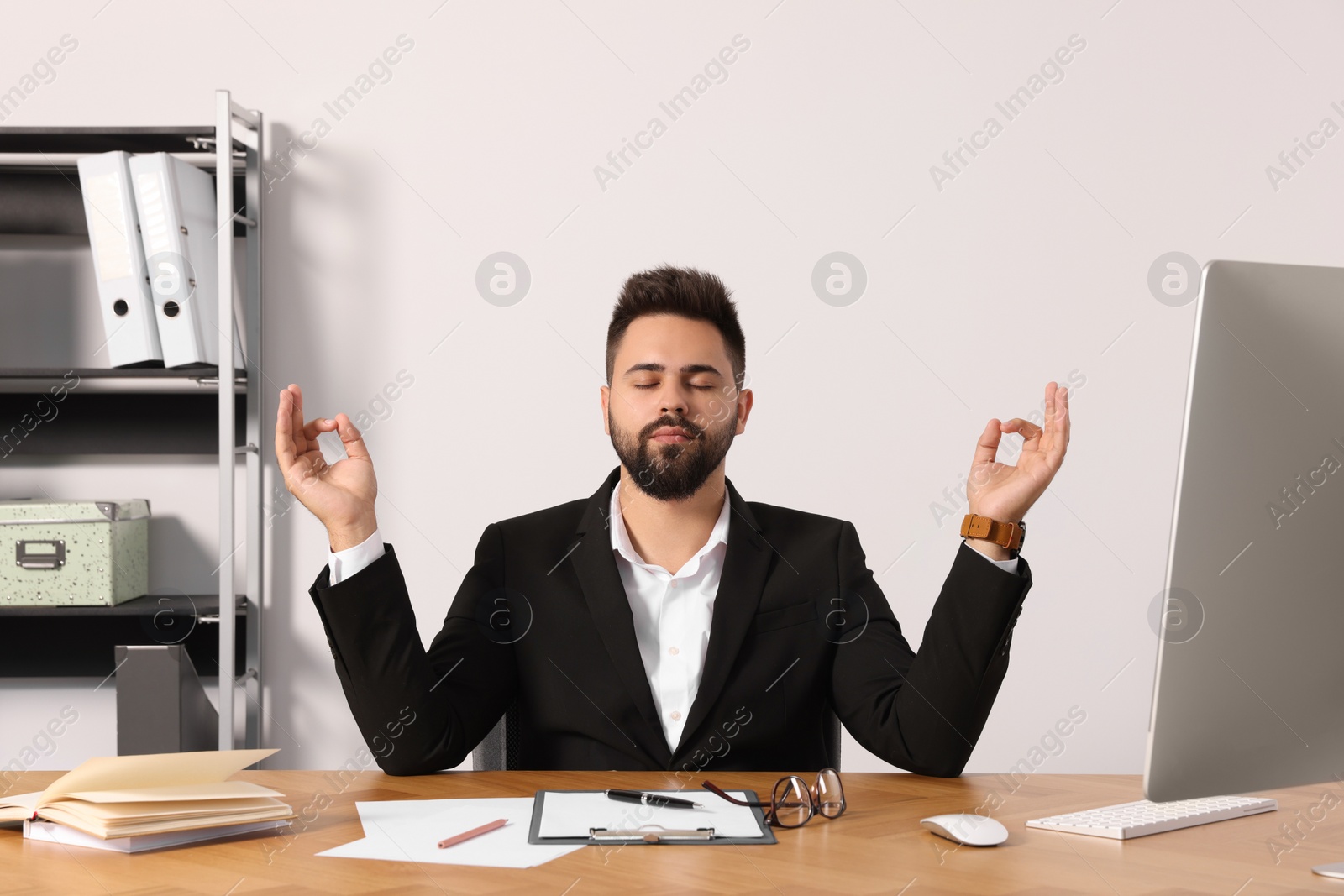 Photo of Young businessman meditating at workplace. Zen concept