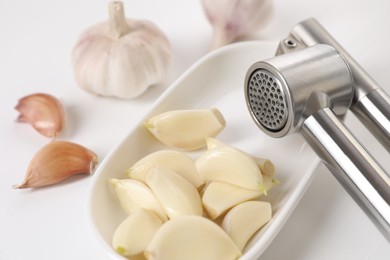 Metal press and garlic on white wooden table, closeup