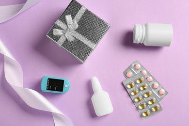 Spray bottle, pills, box and fingertip pulse oximeter on violet background, flat lay. Medical gift