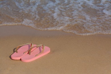 Photo of Stylish flip flops on sandy beach near sea, space for text