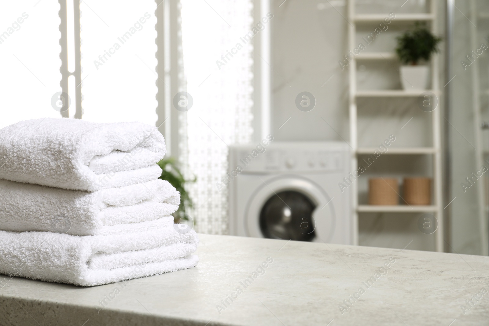 Photo of Stack of clean towels on table in laundry room. Space for text