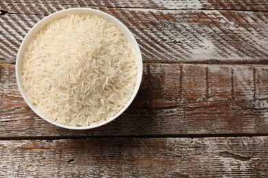 Photo of Raw basmati rice in bowl on wooden table, top view. Space for text