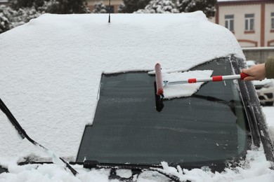 Woman cleaning car windshield from snow with squeegee outdoors, closeup