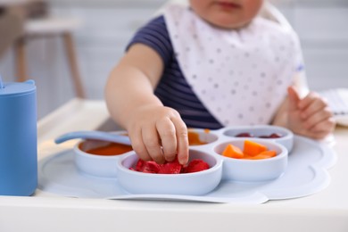 Photo of Little baby eating food in high chair at kitchen, closeup