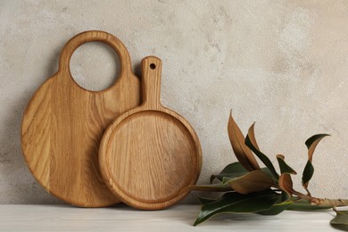 Wooden cutting boards and floral decor on white table near textured wall