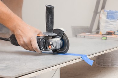 Photo of Worker using saw with circular diamond blade for tile cutting indoors, closeup