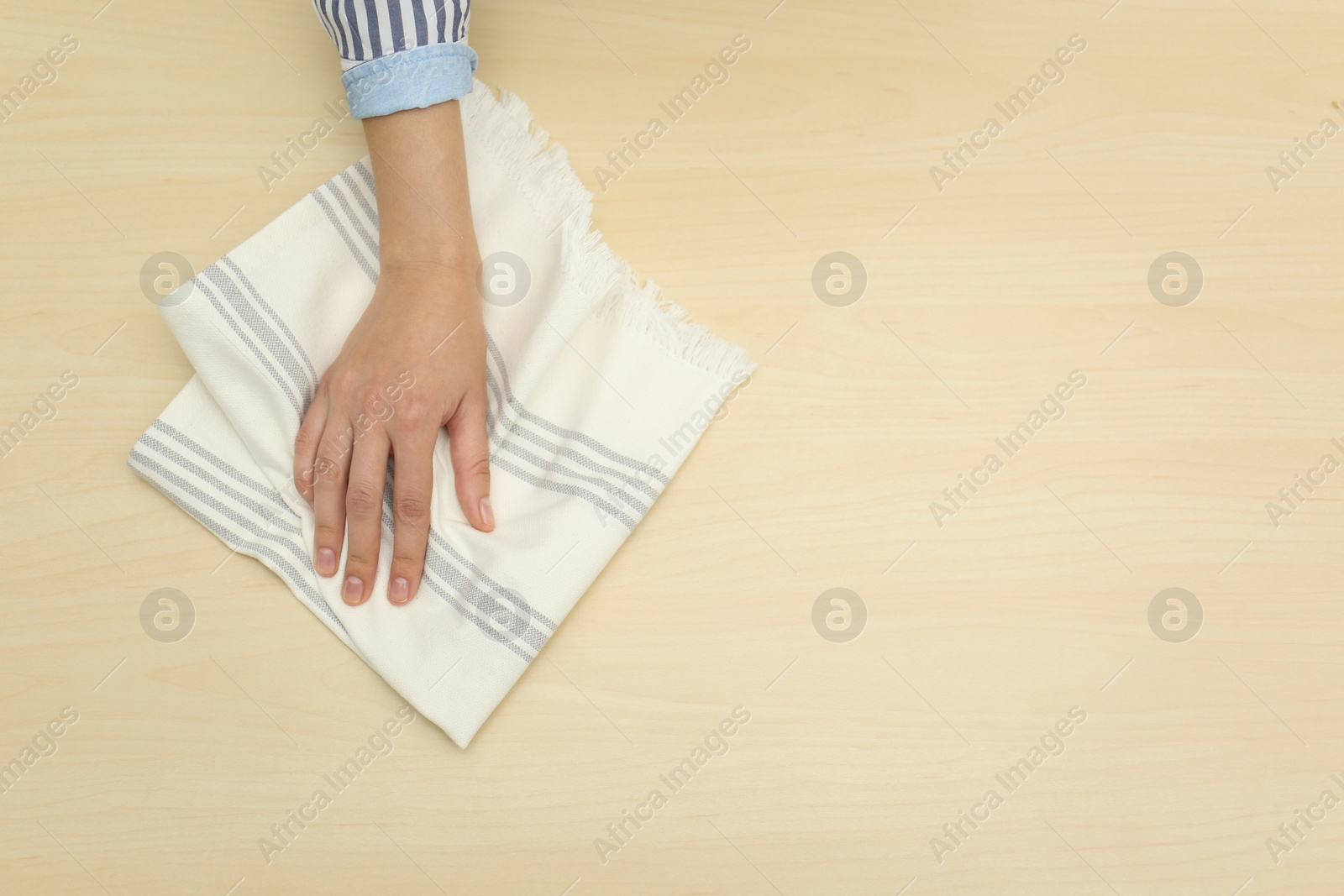 Photo of Woman wiping wooden table with kitchen towel, top view. Space for text