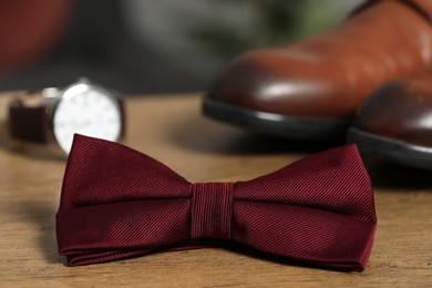 Photo of Stylish burgundy bow tie, wristwatch and shoes on wooden table, closeup