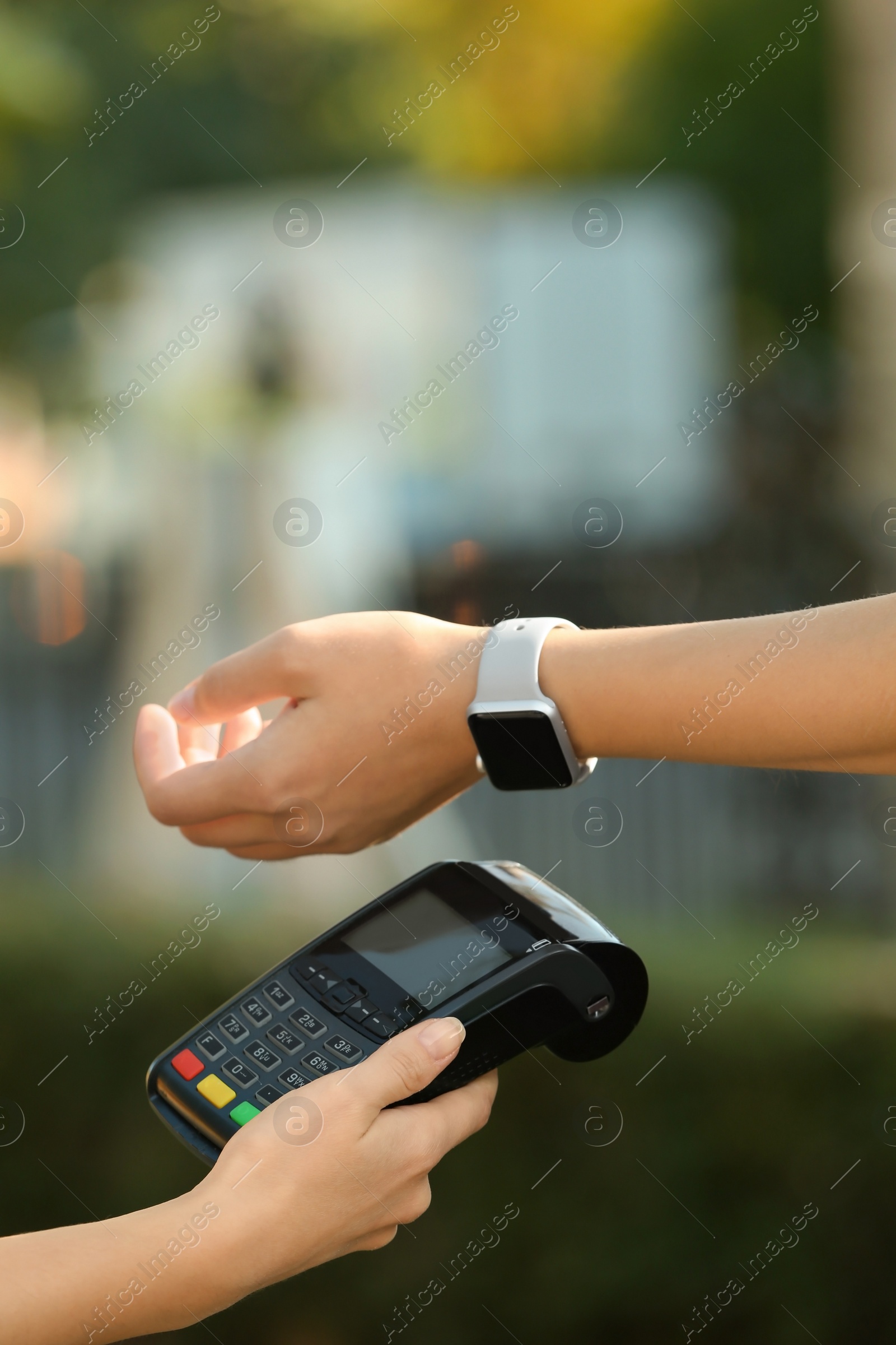 Photo of Woman using terminal for contactless payment with smart watch outdoors