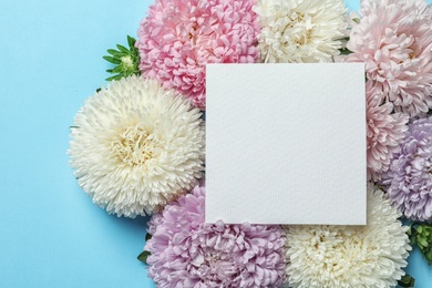 Beautiful aster flowers with sheet of paper on color background, top view. Space for text