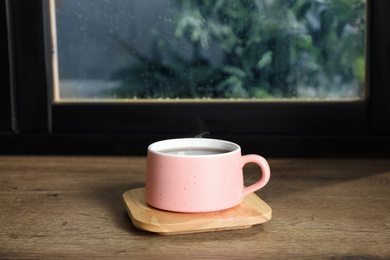 Photo of Cup of hot drink on window sill against glass with rain drops, space for text