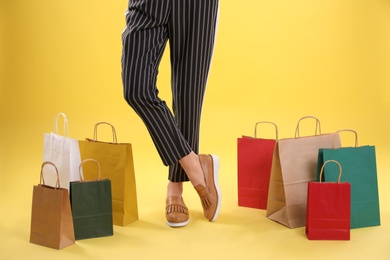 Photo of Young woman with shopping bags on color background, closeup of legs