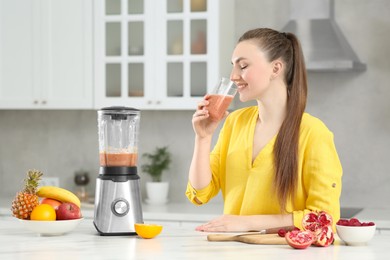 Beautiful young woman with delicious smoothie in kitchen