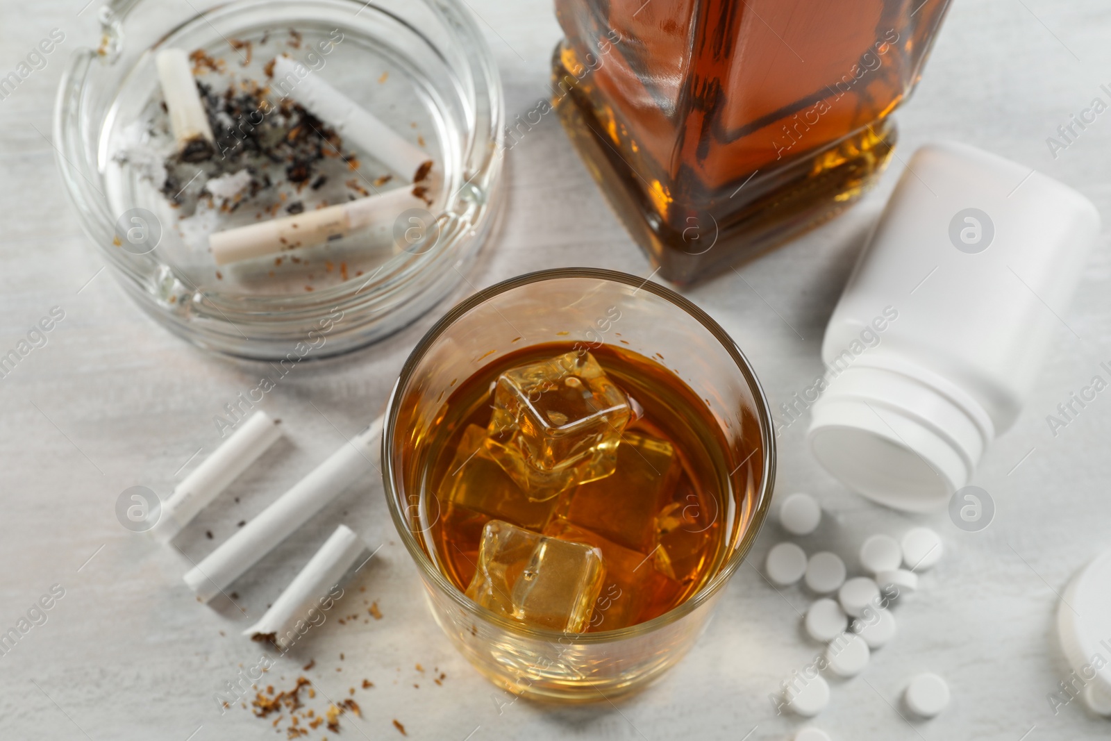 Photo of Alcohol and drug addiction. Whiskey in glass, cigarettes and pills on white table, above view