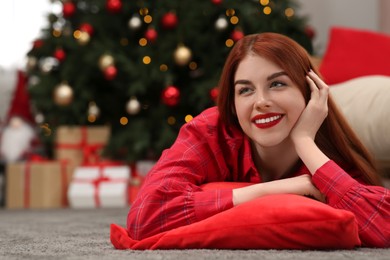 Photo of Beautiful young woman lying on floor near Christmas tree at home, space for text