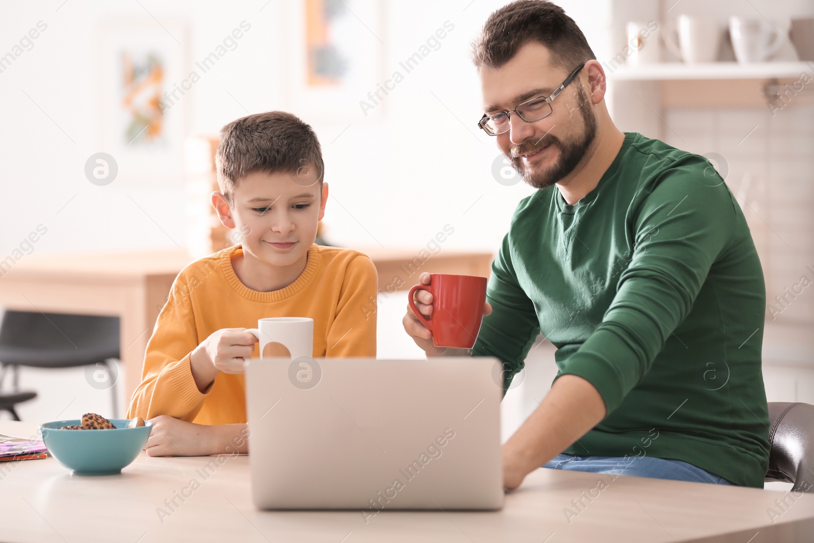 Photo of Little boy and his dad using laptop in kitchen