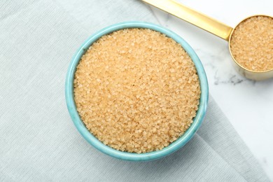 Brown sugar in bowl and scoop on white marble table, top view