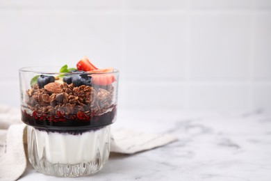 Photo of Tasty granola with berries, jam and yogurt in glass on white marble table, space for text