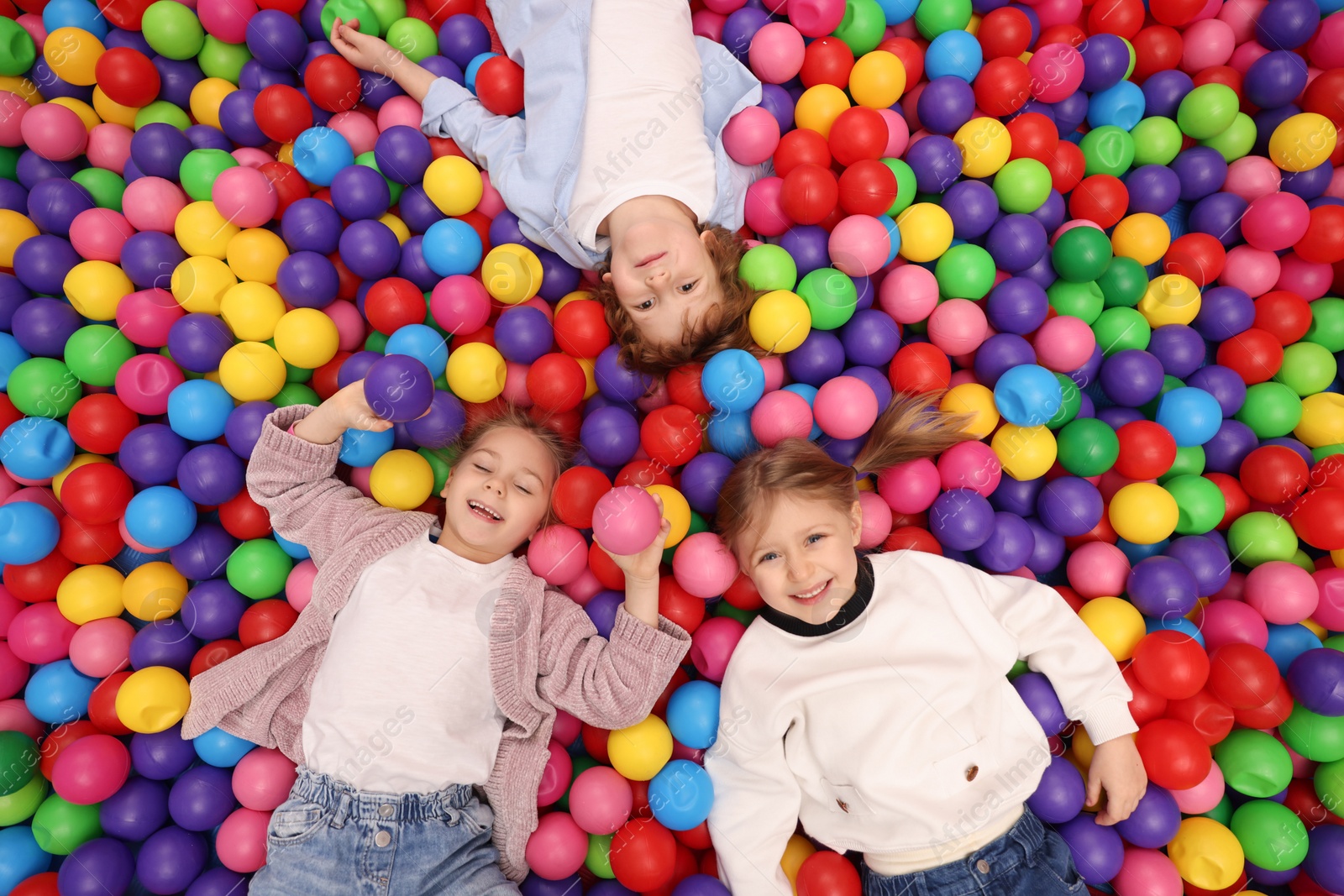 Photo of Happy little kids lying on many colorful balls, top view