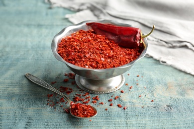 Photo of Bowl with crushed chili pepper and pod on wooden background