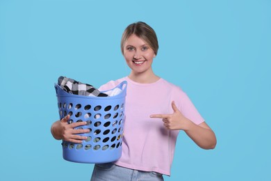 Photo of Happy woman with basket full of laundry on light blue background