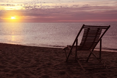 Photo of Wooden deck chair on sandy beach at sunset. Summer vacation