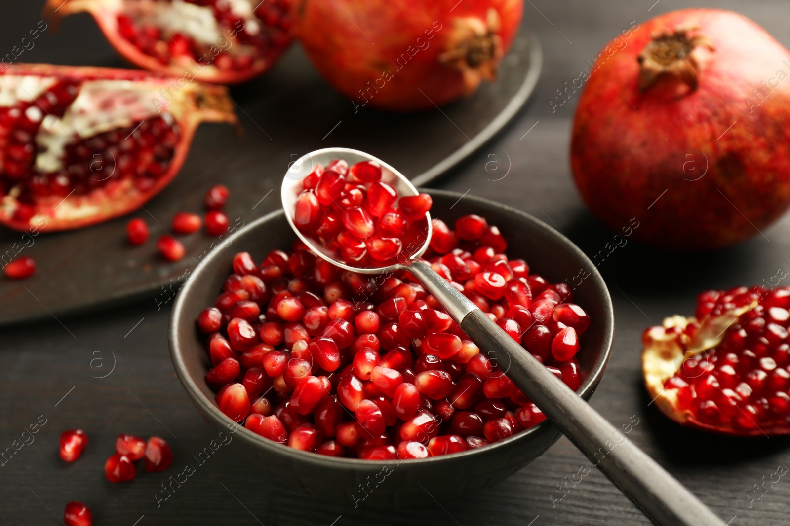 Photo of Tasty ripe pomegranates and grains on dark wooden table, closeup