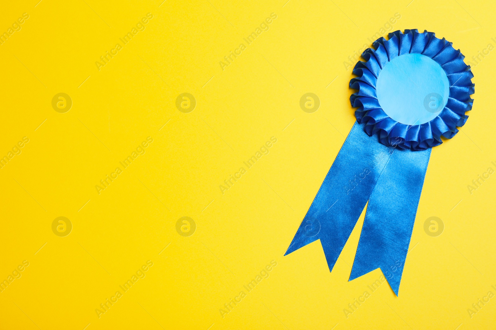 Photo of Blue award ribbon on yellow background, top view. Space for text