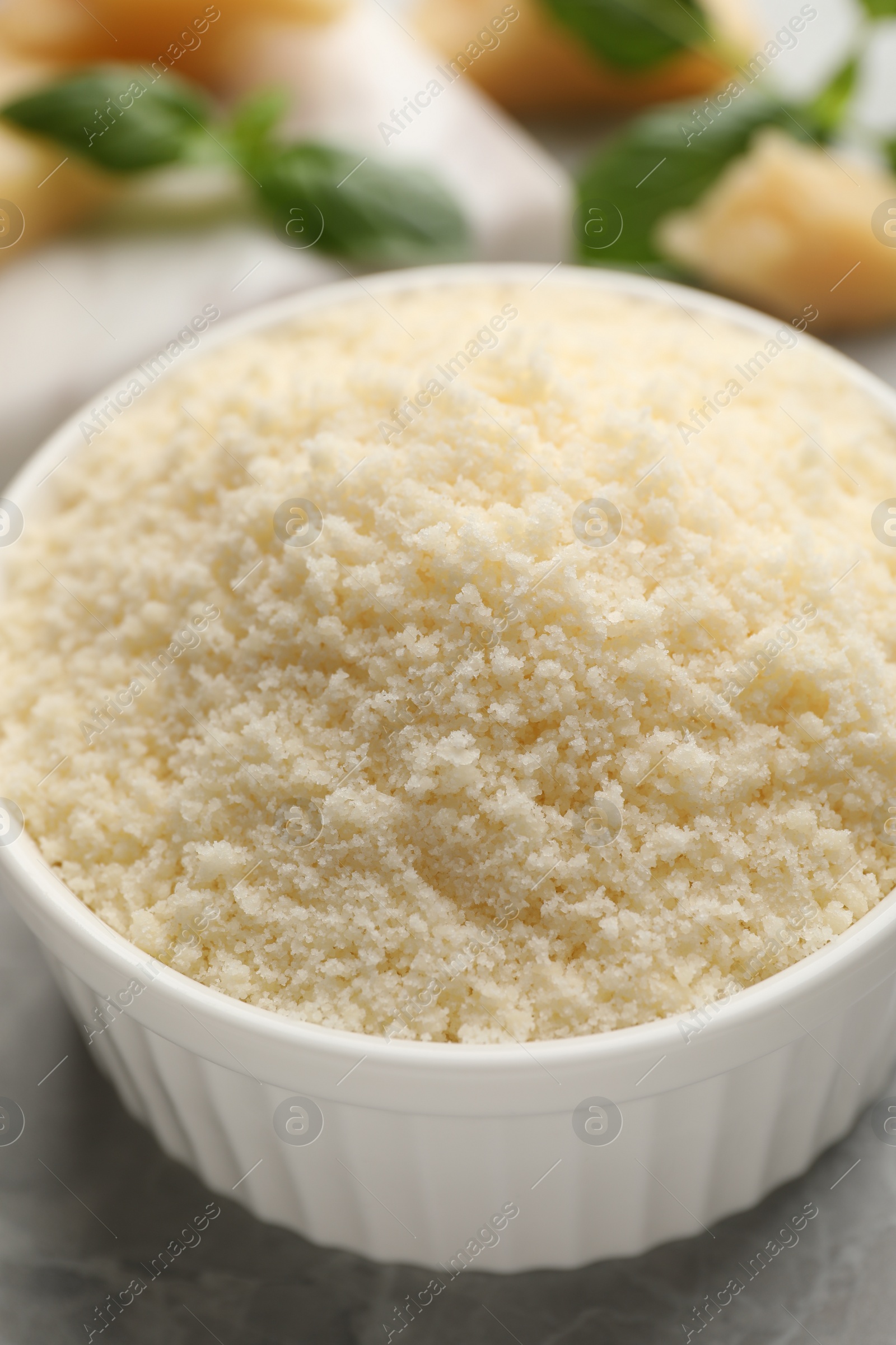 Photo of Bowl with grated parmesan cheese on light table, closeup