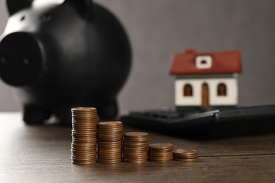 Photo of House model, piggy bank, calculator and stacked coins on wooden table, selective focus