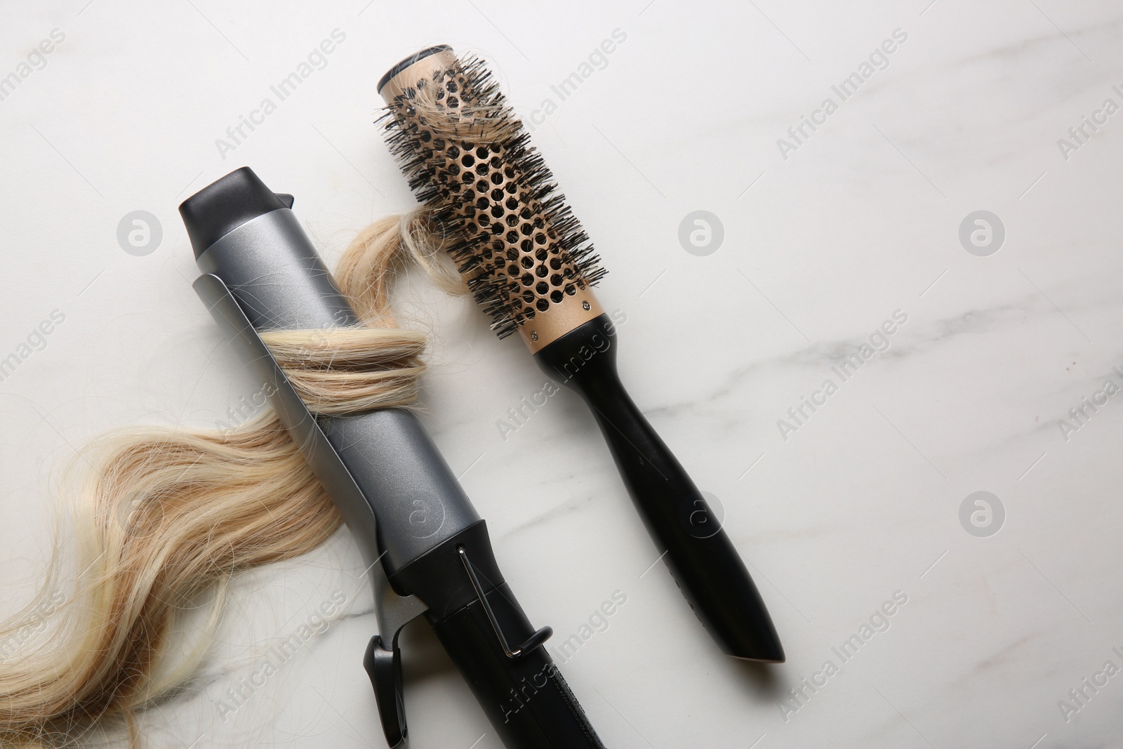 Photo of Curling iron and round brush with blonde hair lock on white marble background, flat lay. Space for text