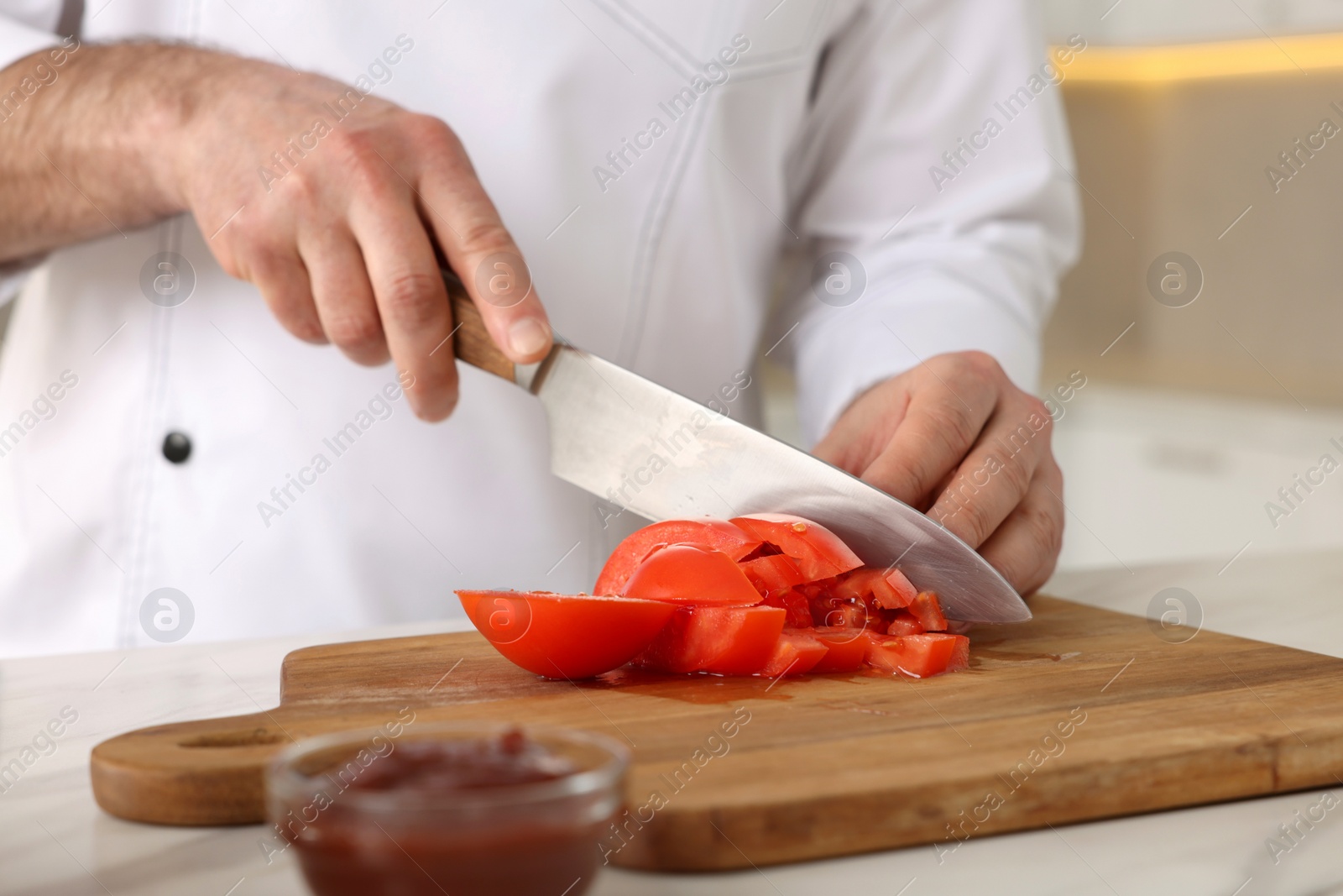 Photo of Professional chef cutting tomatoes at white marble table indoors, closeup