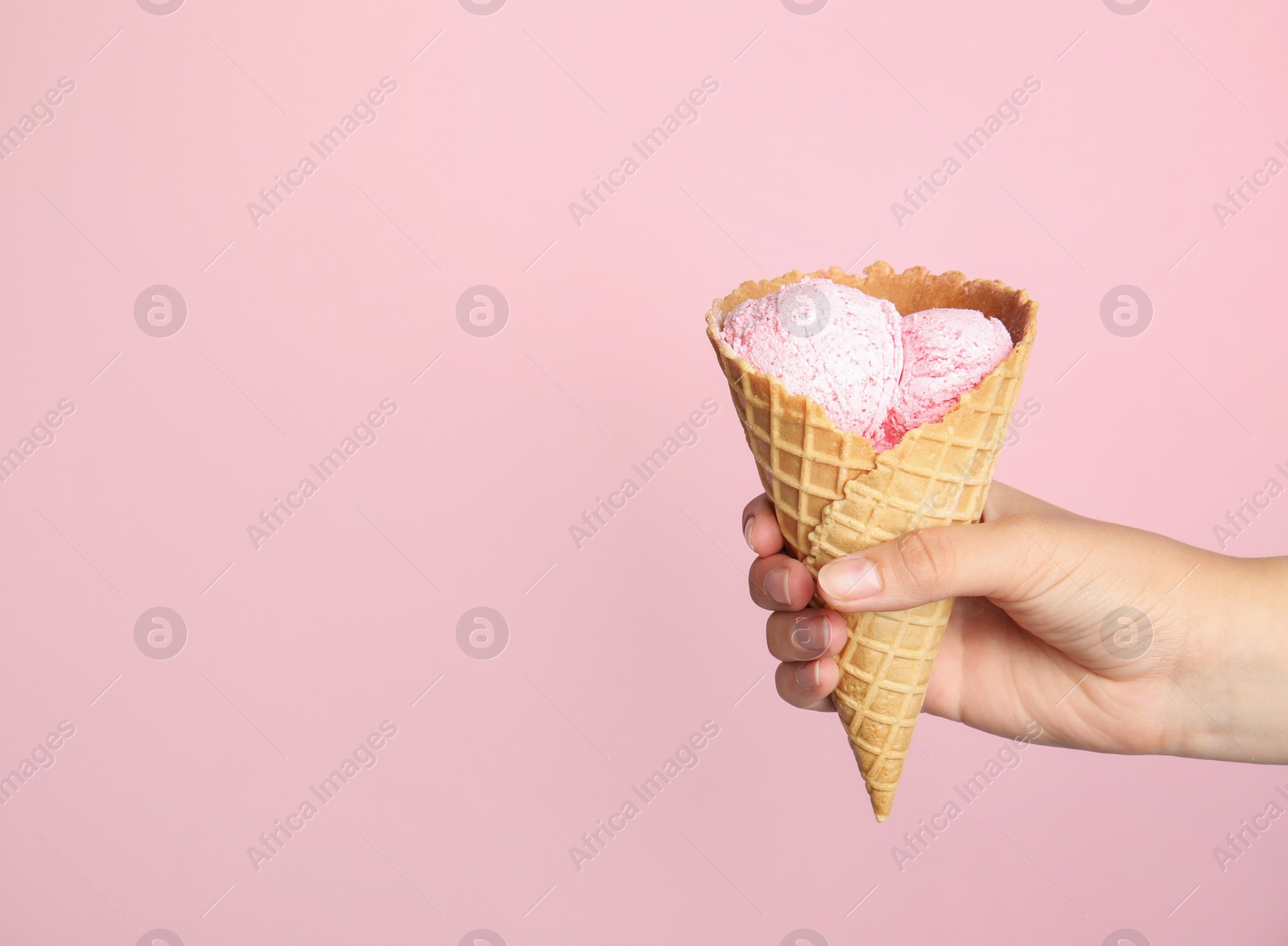 Photo of Woman holding delicious ice cream in wafer cone on pink background, closeup. Space for text