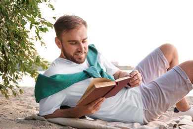 Photo of Young man reading book on sandy beach near sea