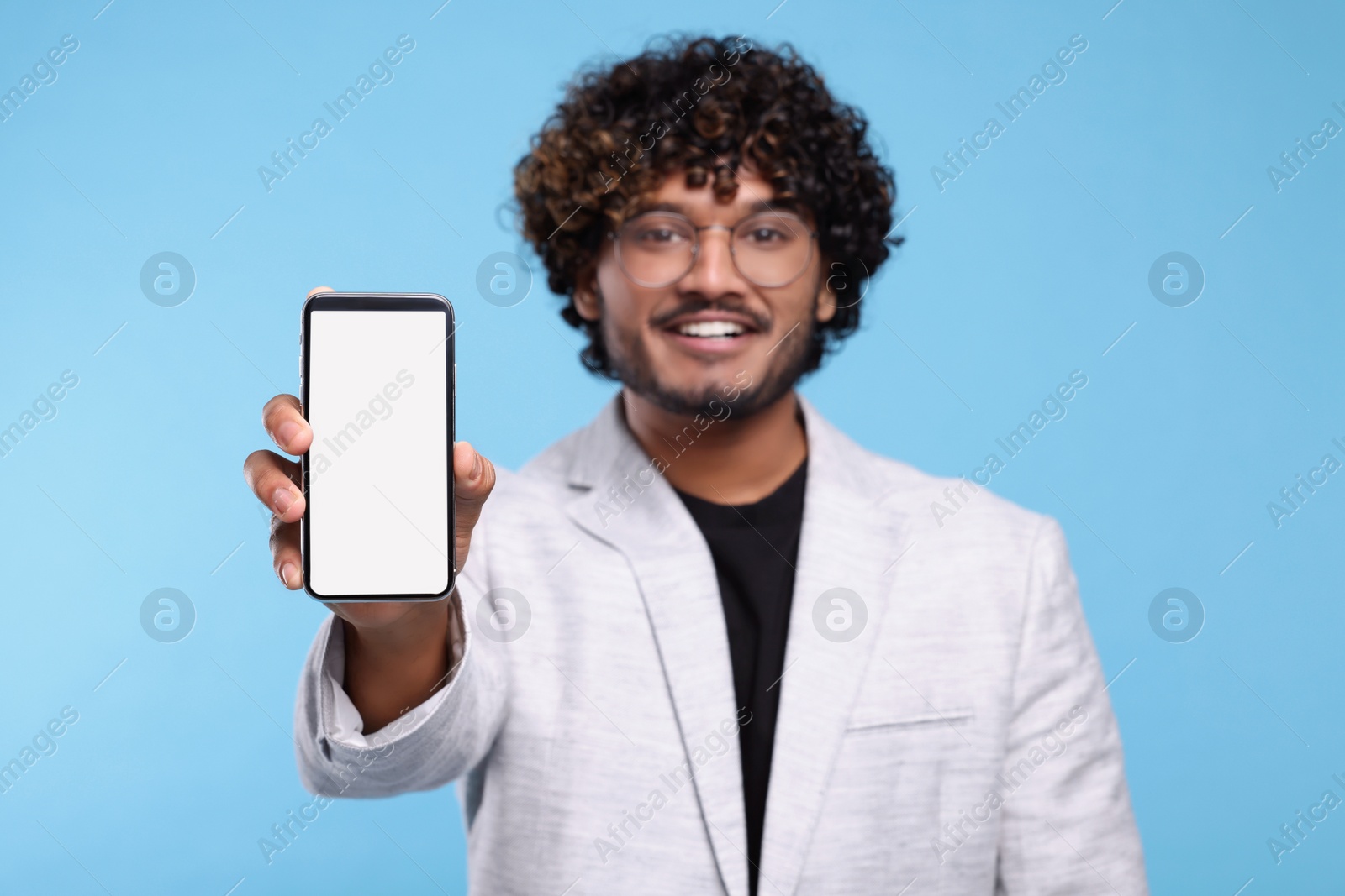 Photo of Handsome smiling man showing smartphone on light blue background, selective focus