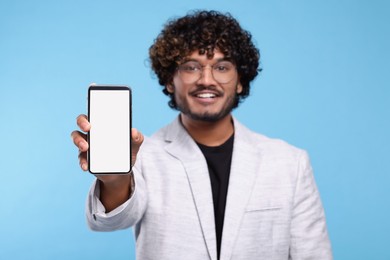 Handsome smiling man showing smartphone on light blue background, selective focus