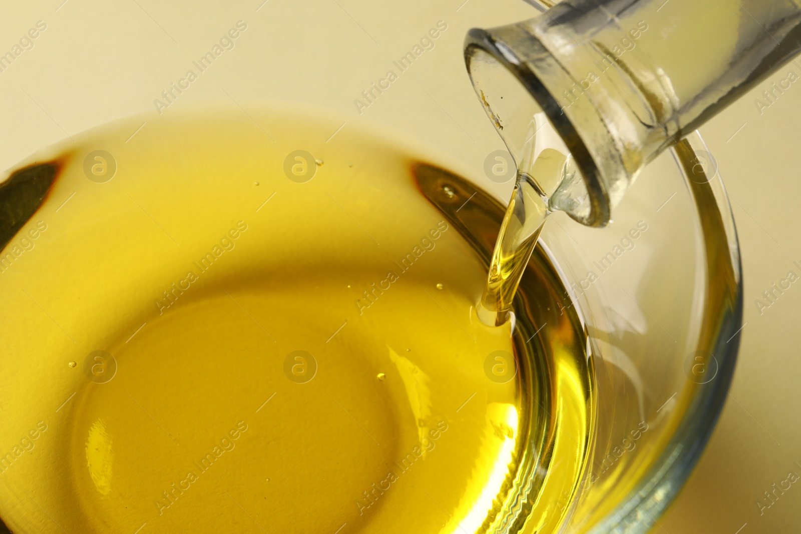 Photo of Pouring cooking oil from bottle into bowl on white background, closeup