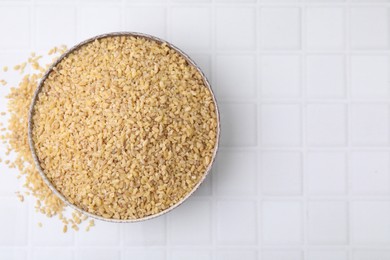 Photo of Raw bulgur in bowl on white tiled table, top view. Space for text
