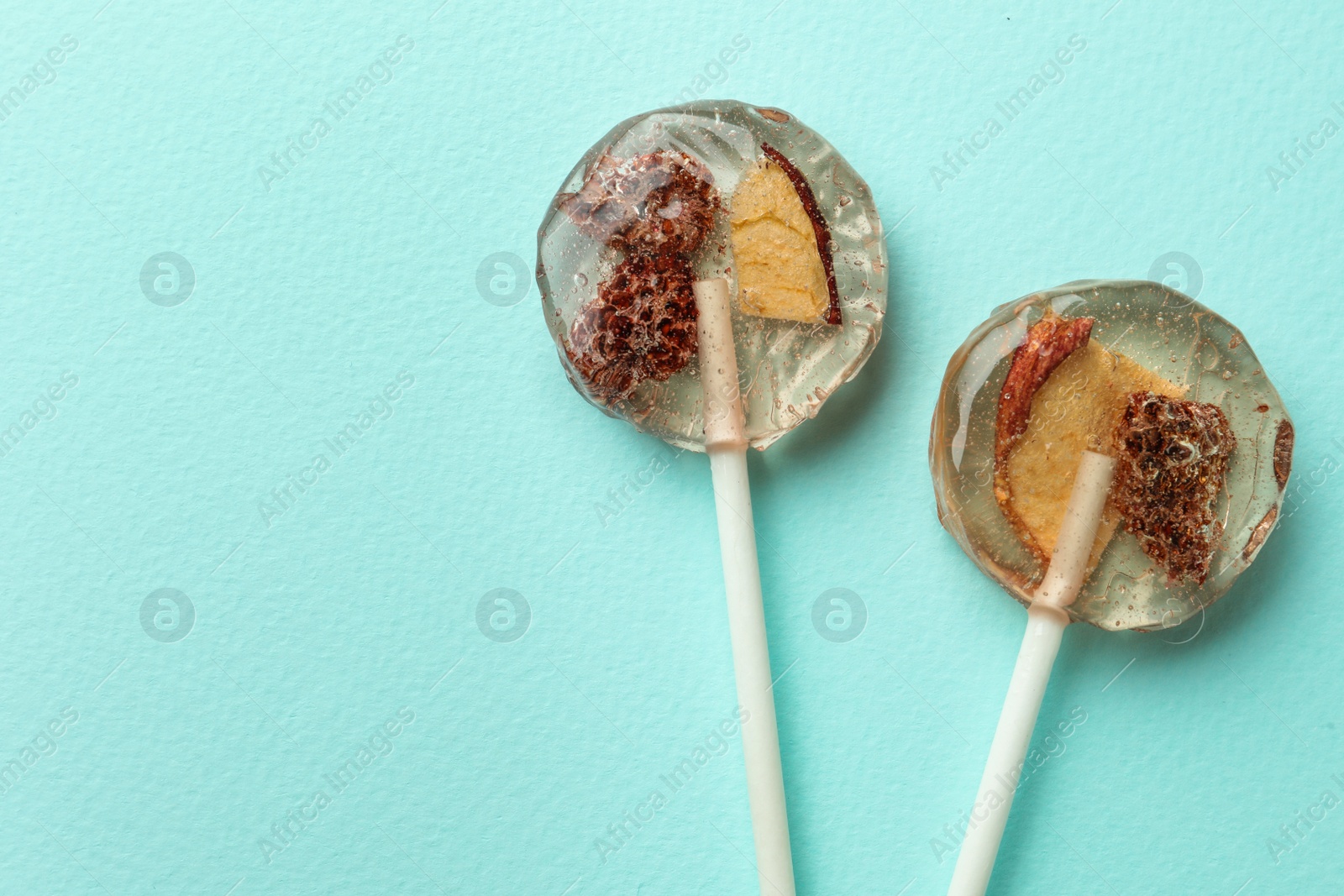 Photo of Sweet colorful lollipops with berries on turquoise background, flat lay. Space for text