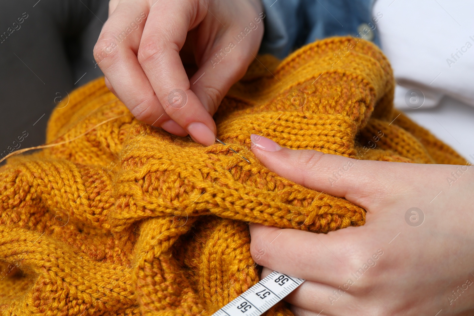 Photo of Woman sewing sweater with needle, closeup view