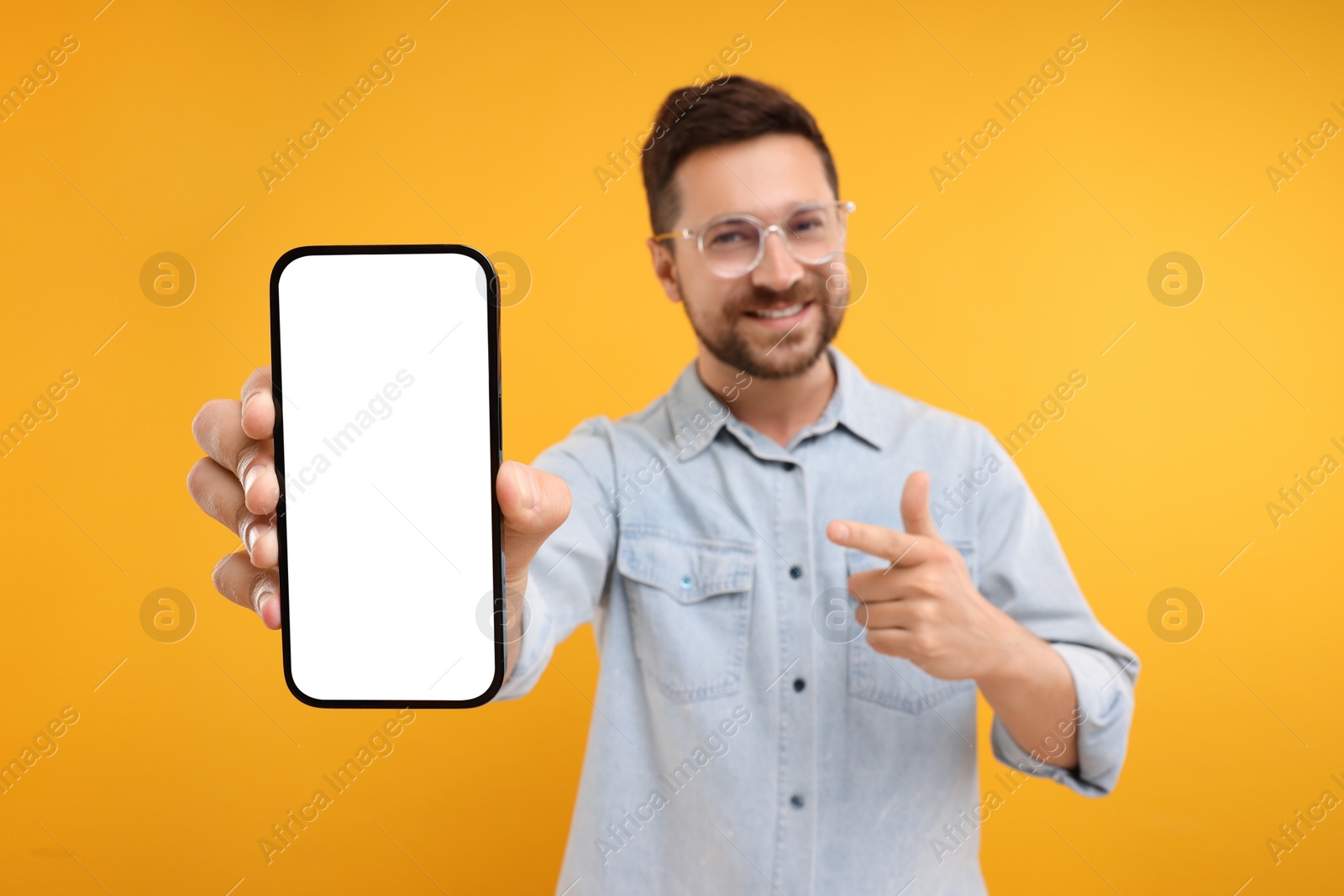 Photo of Handsome man showing smartphone in hand and pointing at it on yellow background, selective focus. Mockup for design