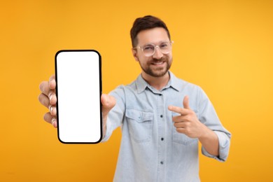 Handsome man showing smartphone in hand and pointing at it on yellow background, selective focus. Mockup for design