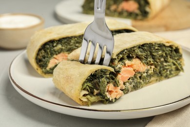 Photo of Eating delicious strudel with salmon and spinach at light grey table, closeup