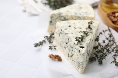 Tasty blue cheese with thyme on white tiled table, closeup. Space for text