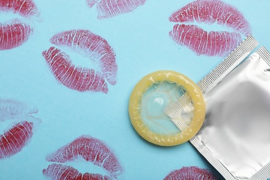 Photo of Condom with lipstick kiss marks on light blue background, flat lay. Safe sex