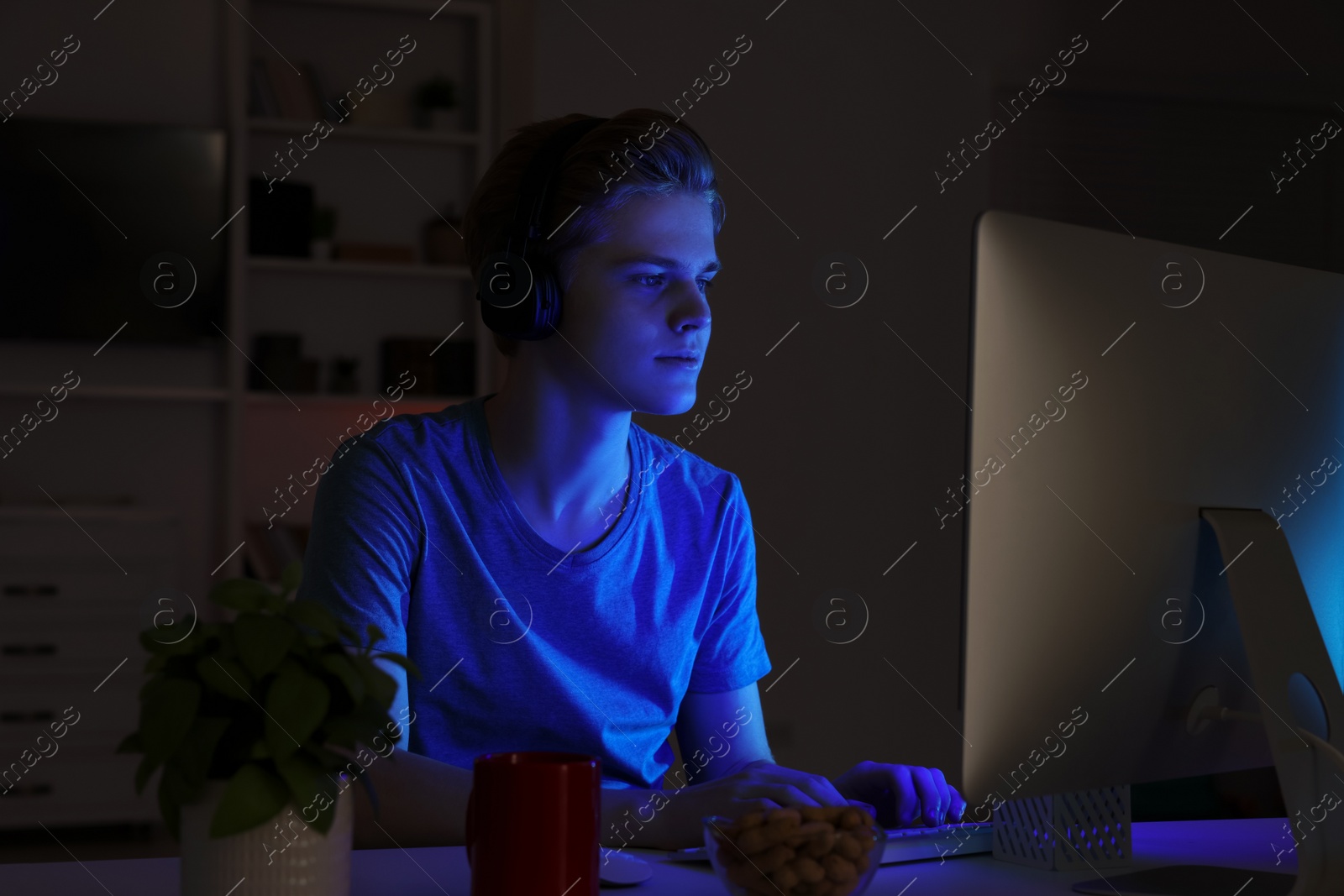 Photo of Teenage boy using computer in bedroom at night. Internet addiction