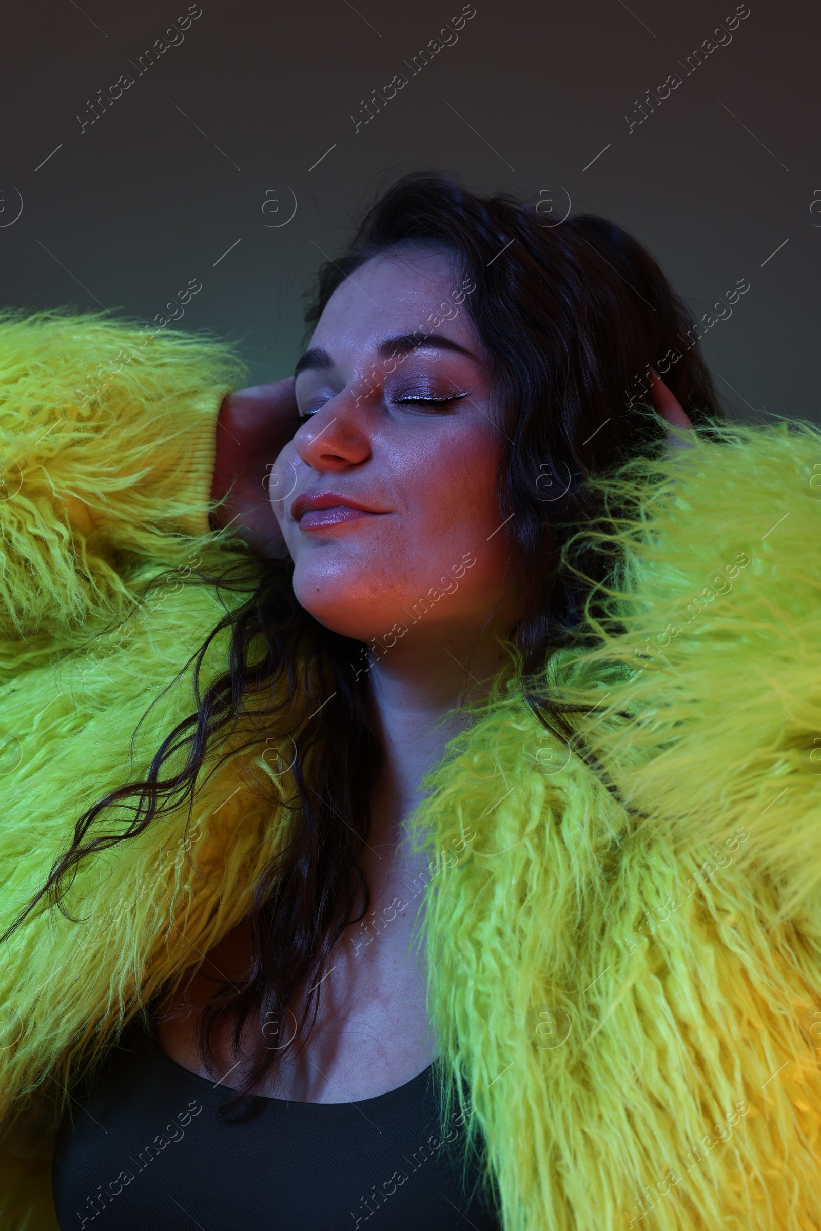 Photo of Portrait of beautiful woman in yellow fur coat on dark background with neon lights