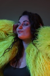 Portrait of beautiful woman in yellow fur coat on dark background with neon lights