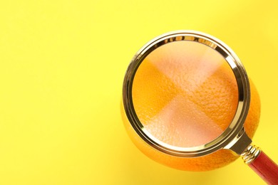 Cellulite problem. Orange and magnifying glass on yellow background, top view. Space for text